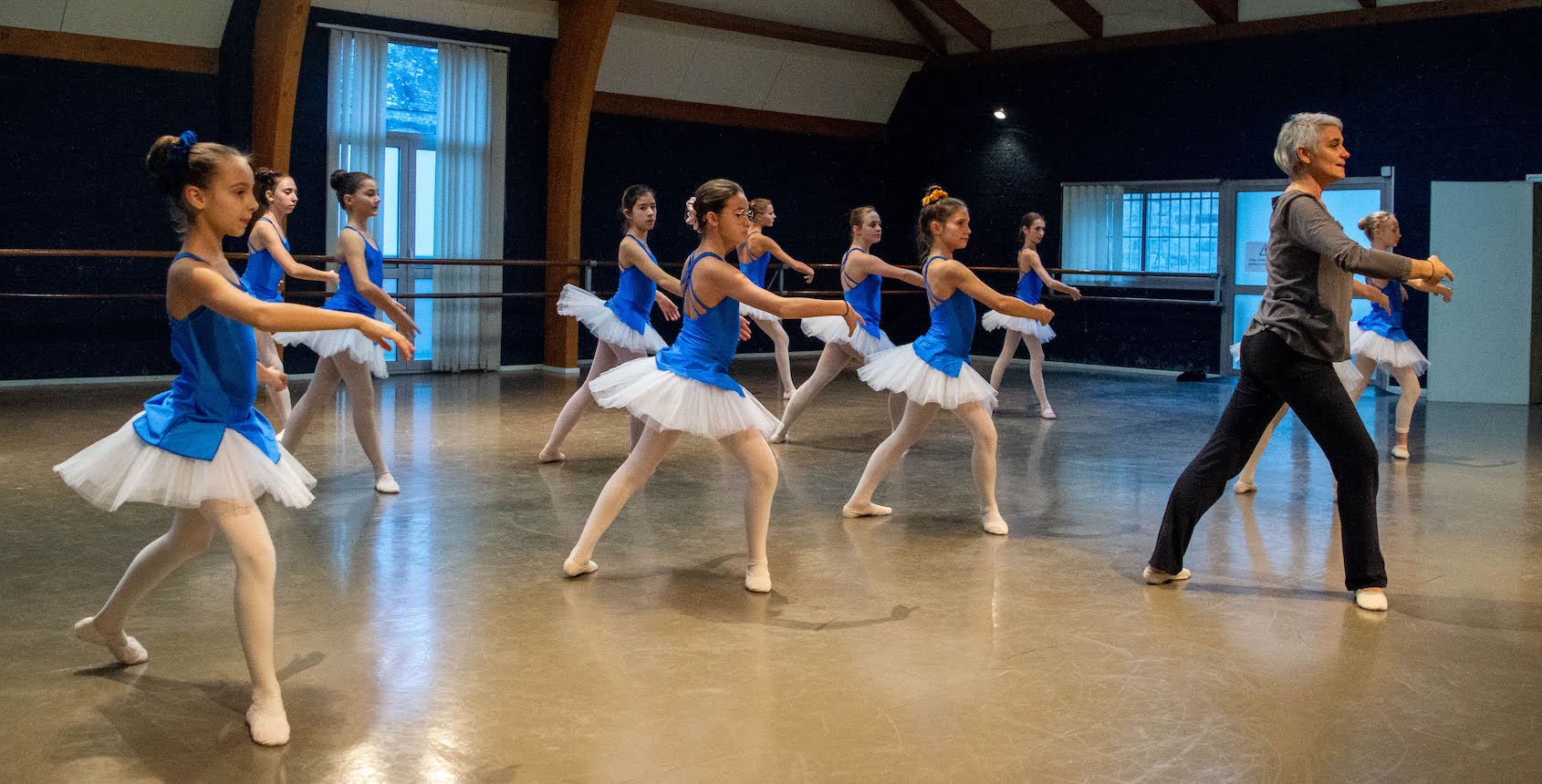 Une professeur de dans et ses élèves faisant des mouvements de danse danc un salle de danse.